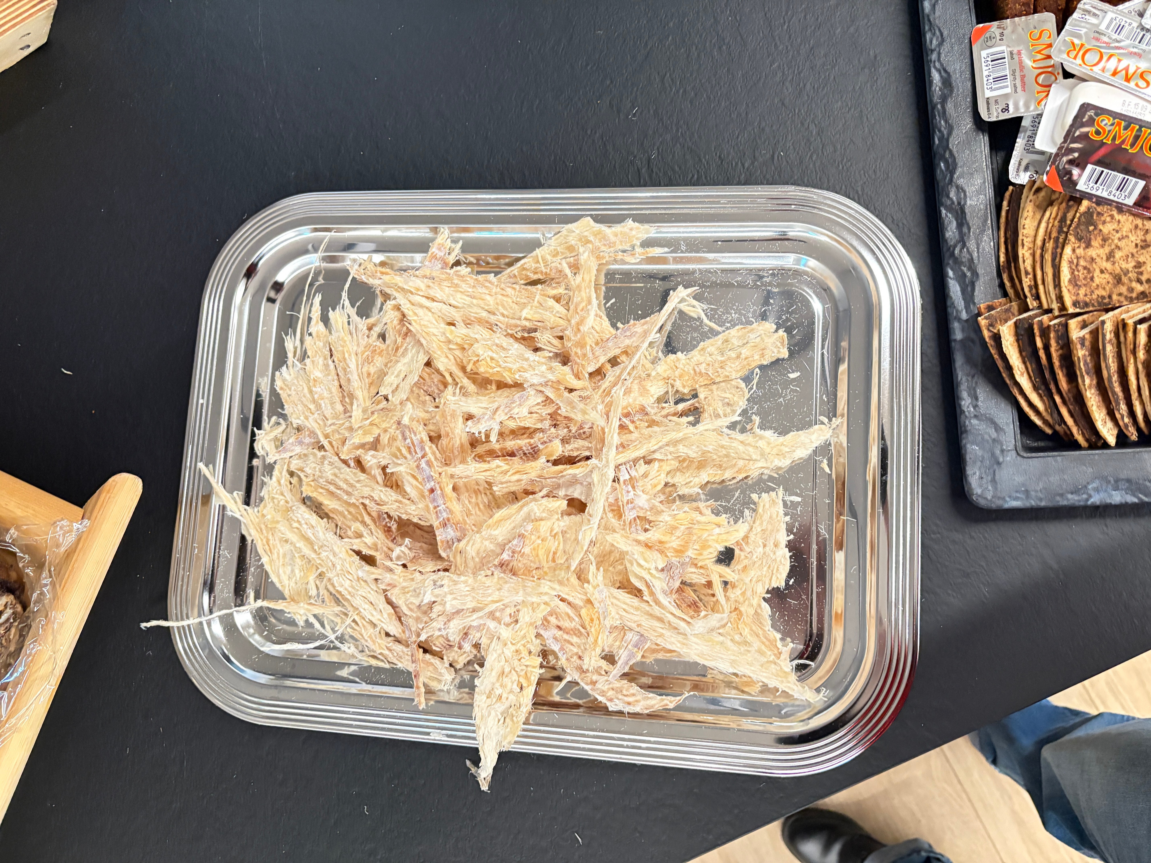 Torn strips of pale dried fish on a metal tray with flatbread behind.