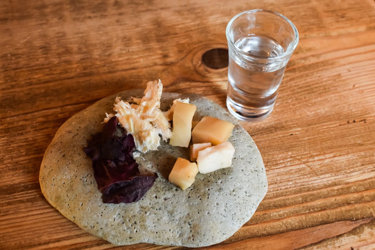 Cubes of hákarl on flatbread beside a shot of clear Brennivín.