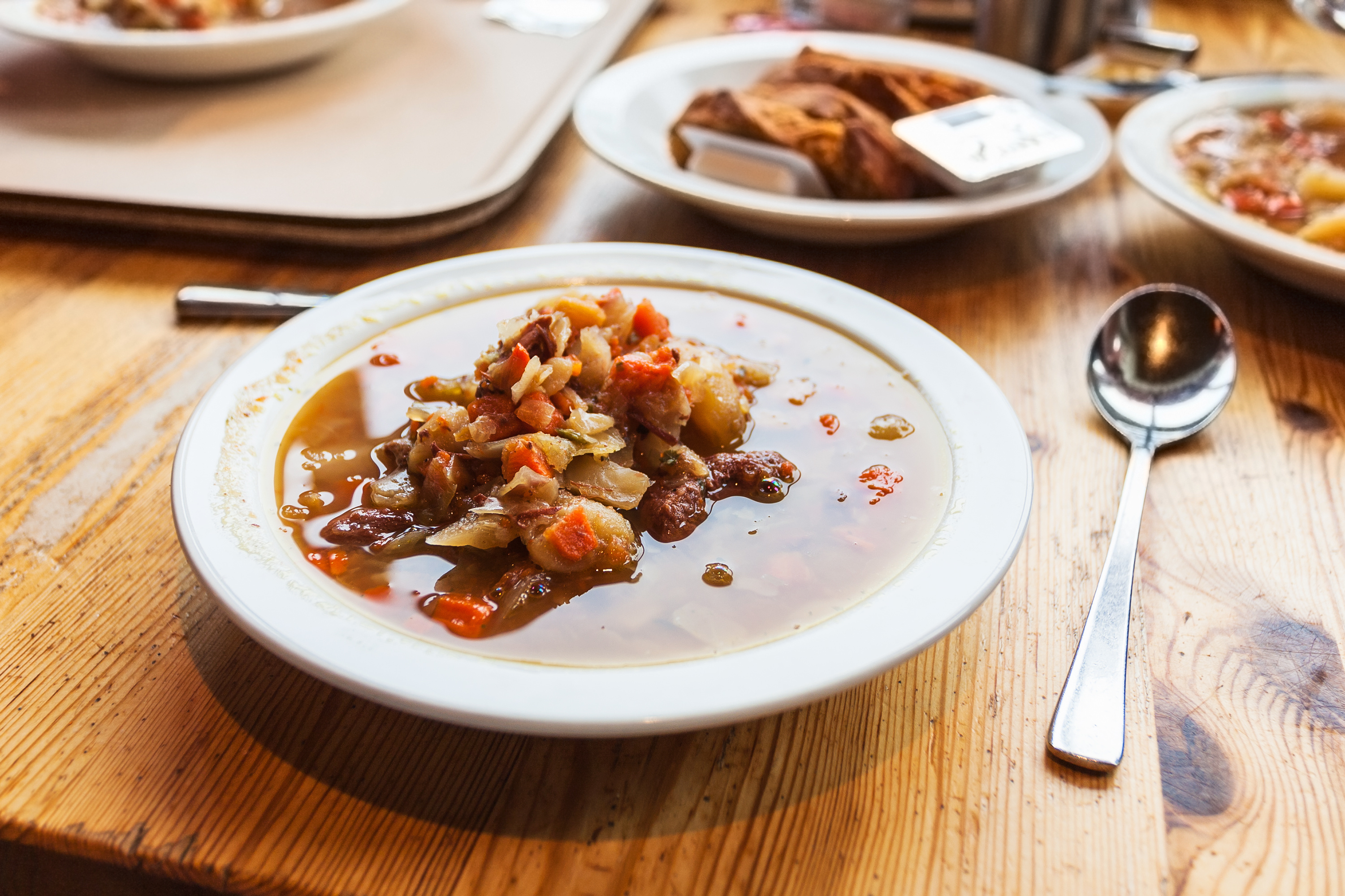 Bowl of Icelandic lamb soup with carrots and potatoes beside a spoon on a wooden table.