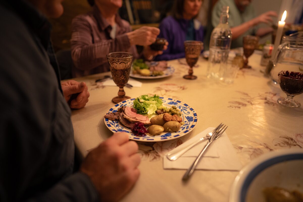 Plate of sliced lamb, potatoes, greens, and red cabbage at a candlelit Icelandic dinner.