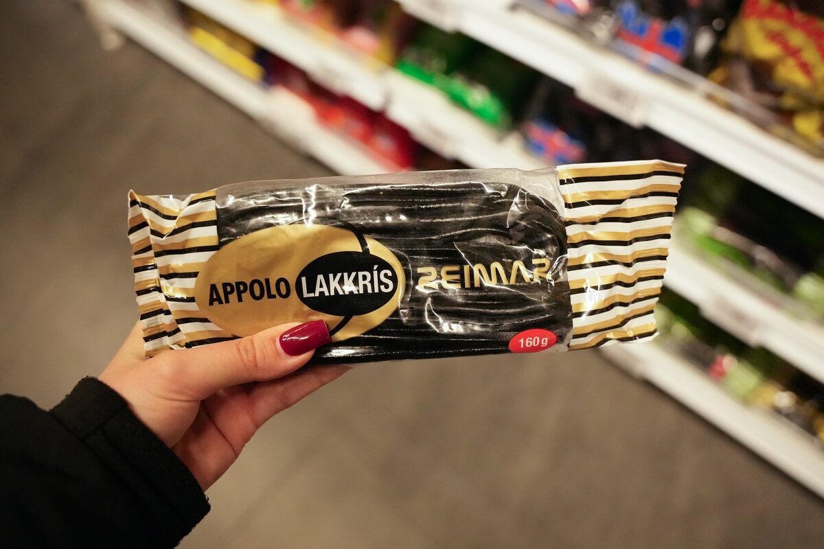Hand holding a bar of Appolo Lakkrís licorice in a supermarket candy aisle.