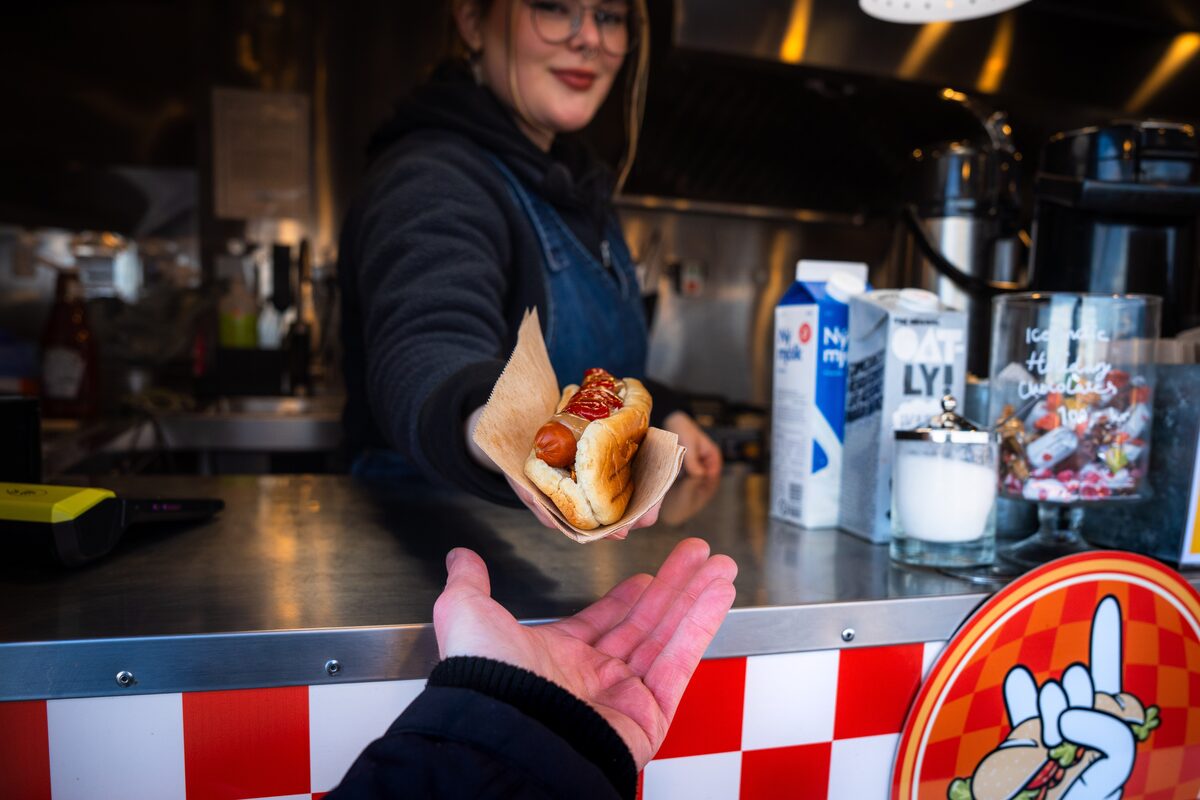 Vendor handing an Icelandic hot dog topped with ketchup to a customer at a food truck.