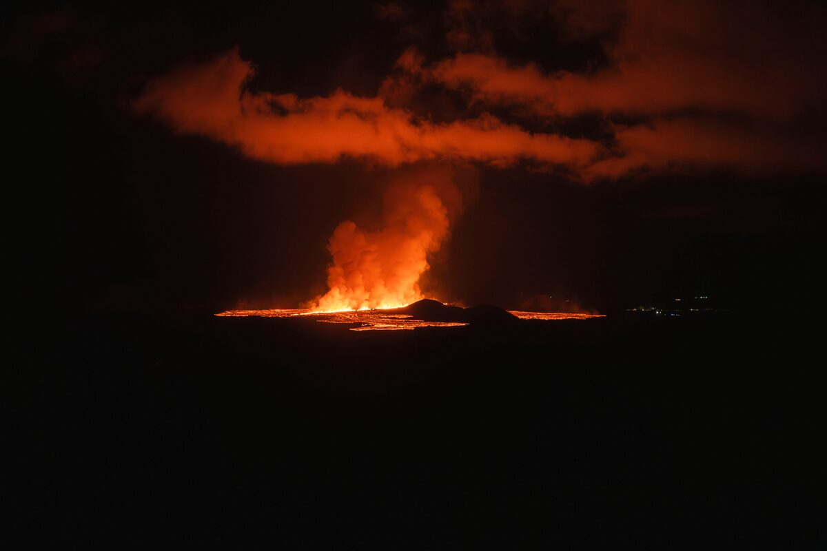 Orange lava glowing at night beneath a tall plume of smoke lit from below in Iceland.