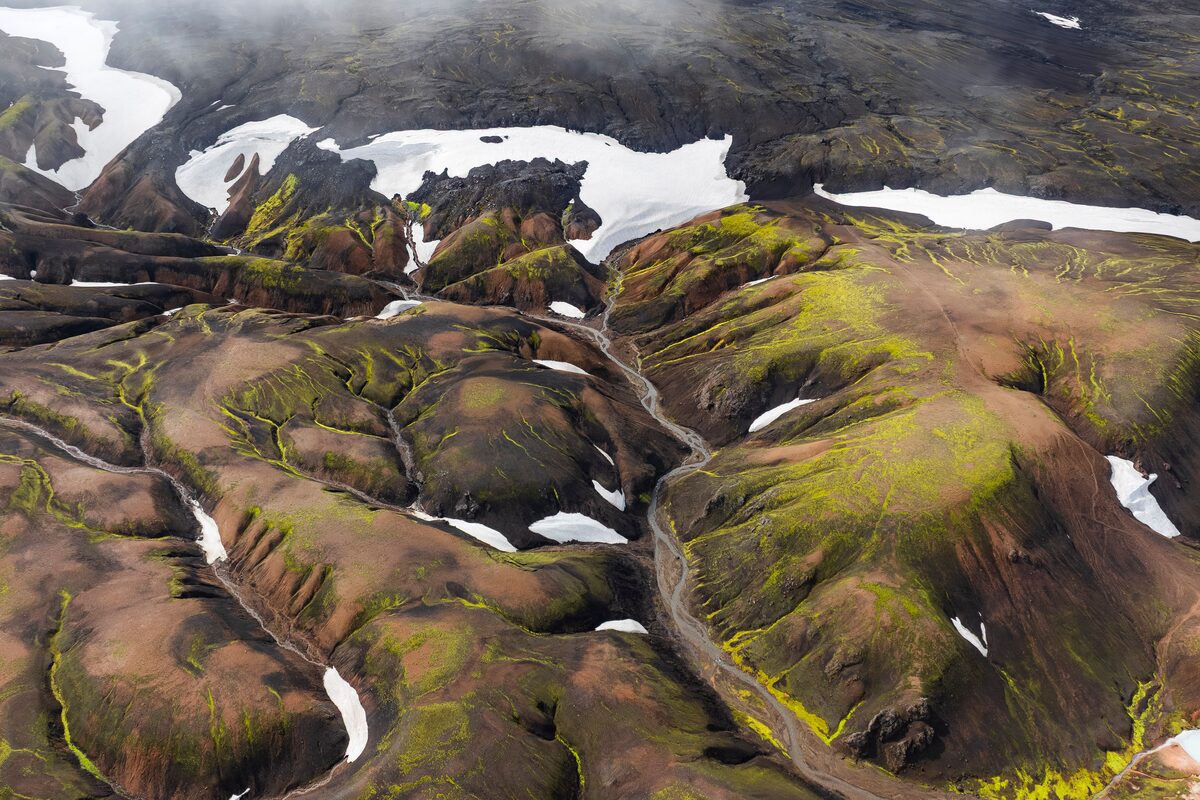 Snow patches and meltwater channels on mossy highland slopes in Iceland, seen from above.