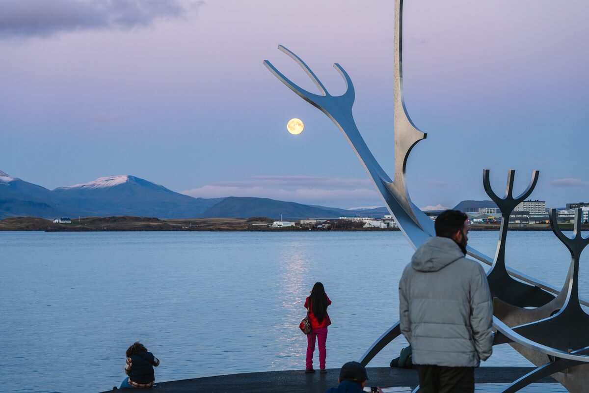 People by the Sun Voyager sculpture on Reykjavík's waterfront, a full moon over the bay.