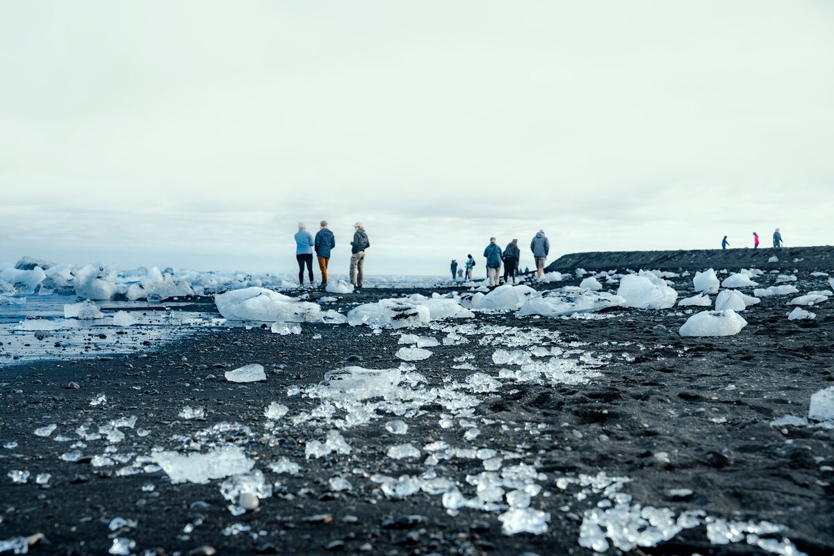 People walking among chunks of ice on a black-sand beach in Iceland.