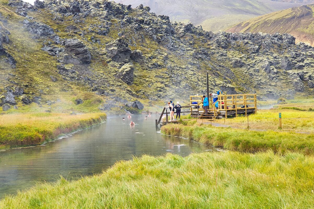 People bathing in a steaming geothermal river at Landmannalaugar, with a wooden changing platform.