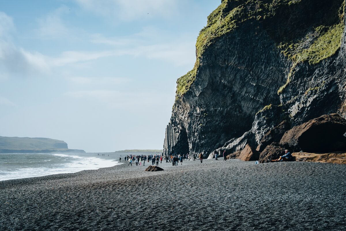 People on the black-sand beach at Reynisfjara below tall basalt cliffs.