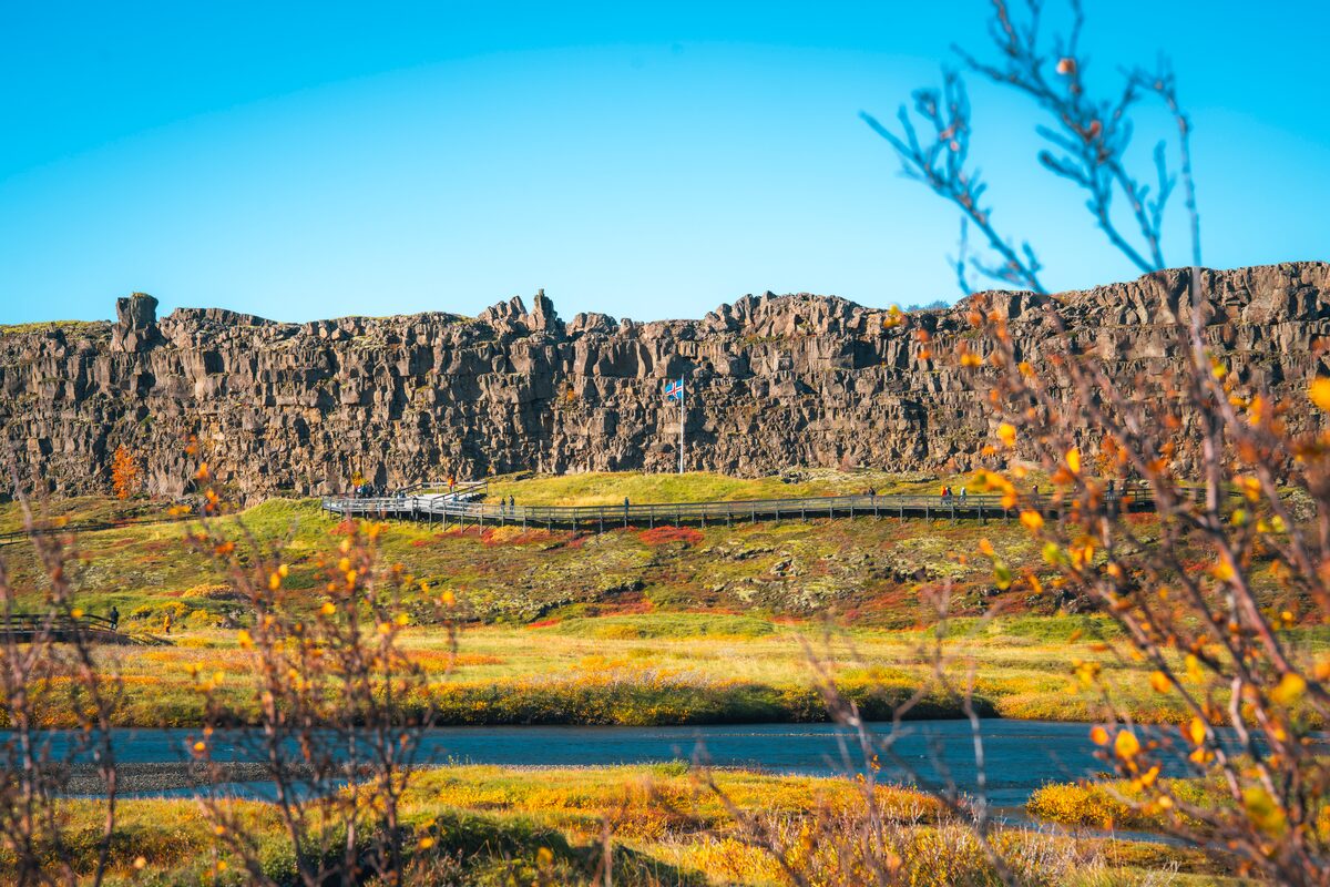 The basalt rift wall at Þingvellir above golden autumn meadows and a still river.