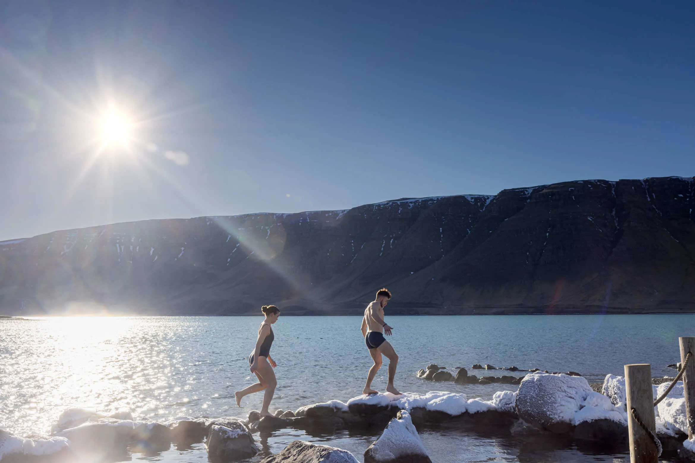 A Couple Walking On Stones In Winter In Hvammsvik Hot Springs in Iceland