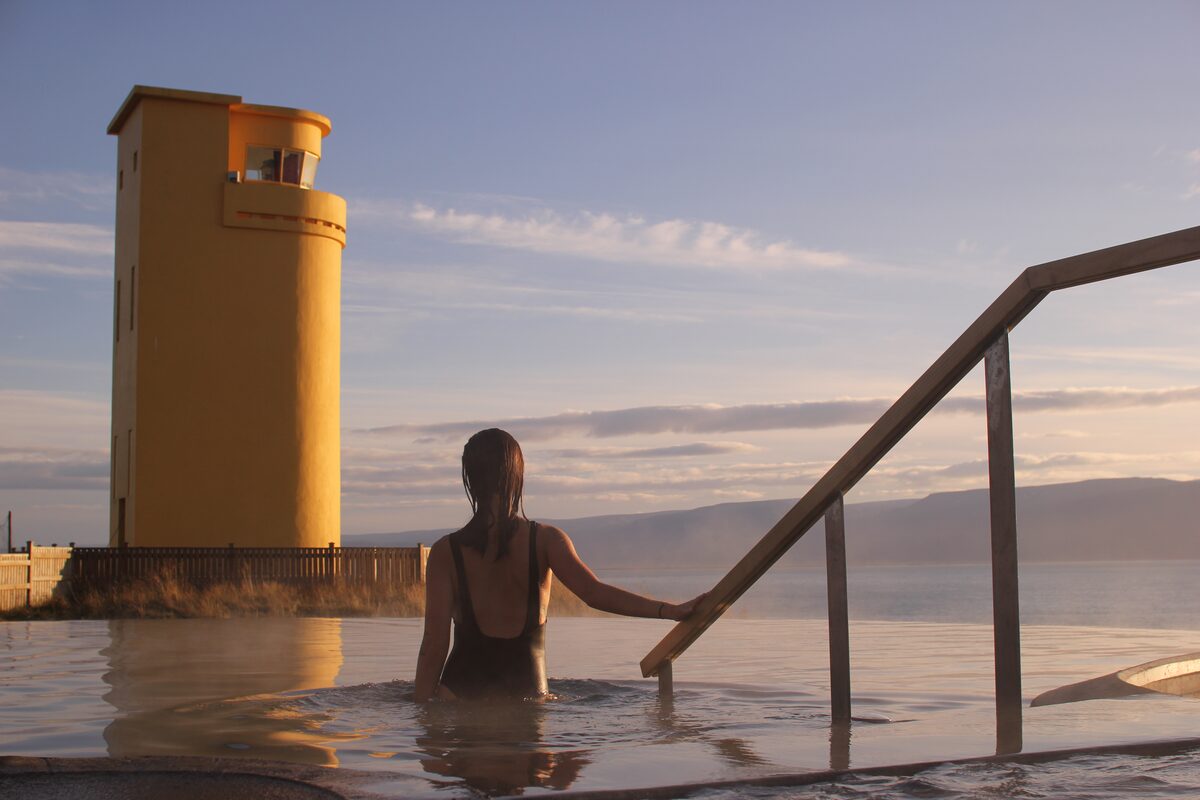 Woman At Geosea Hot Springs With A Yellow Lighthouse In The Background in Iceland
