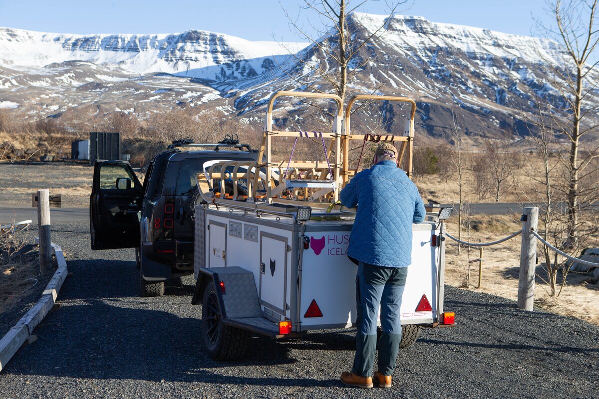A Man Near A Van And Trailer With Sleds On It With Mountains In The Background in Iceland