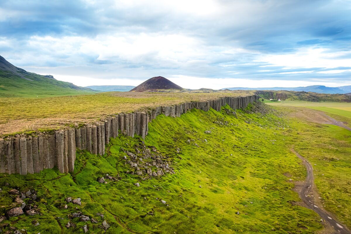 Gerðuberg's row of basalt columns along a green ridge, with a cone-shaped hill behind.
