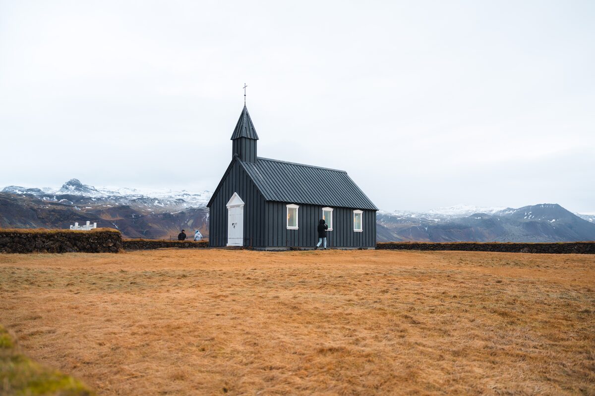Black timber church with a white door and small spire, standing in golden grass at Búðir.