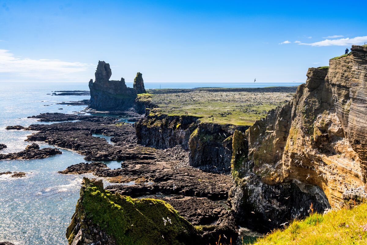 Two rock towers rising from a lava shoreline, with mossy cliffs and blue sea at Lóndrangar.