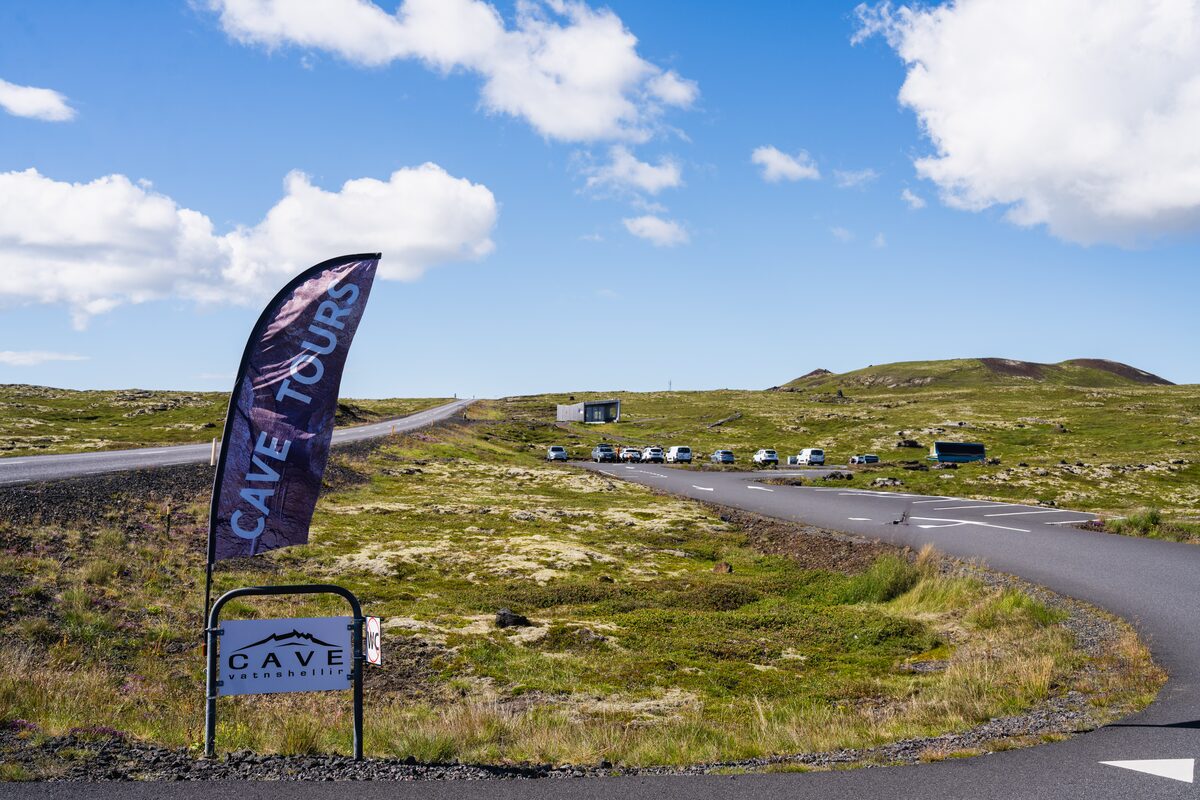 A cave tours banner and sign beside the road at Vatnshellir, with a parking area behind.