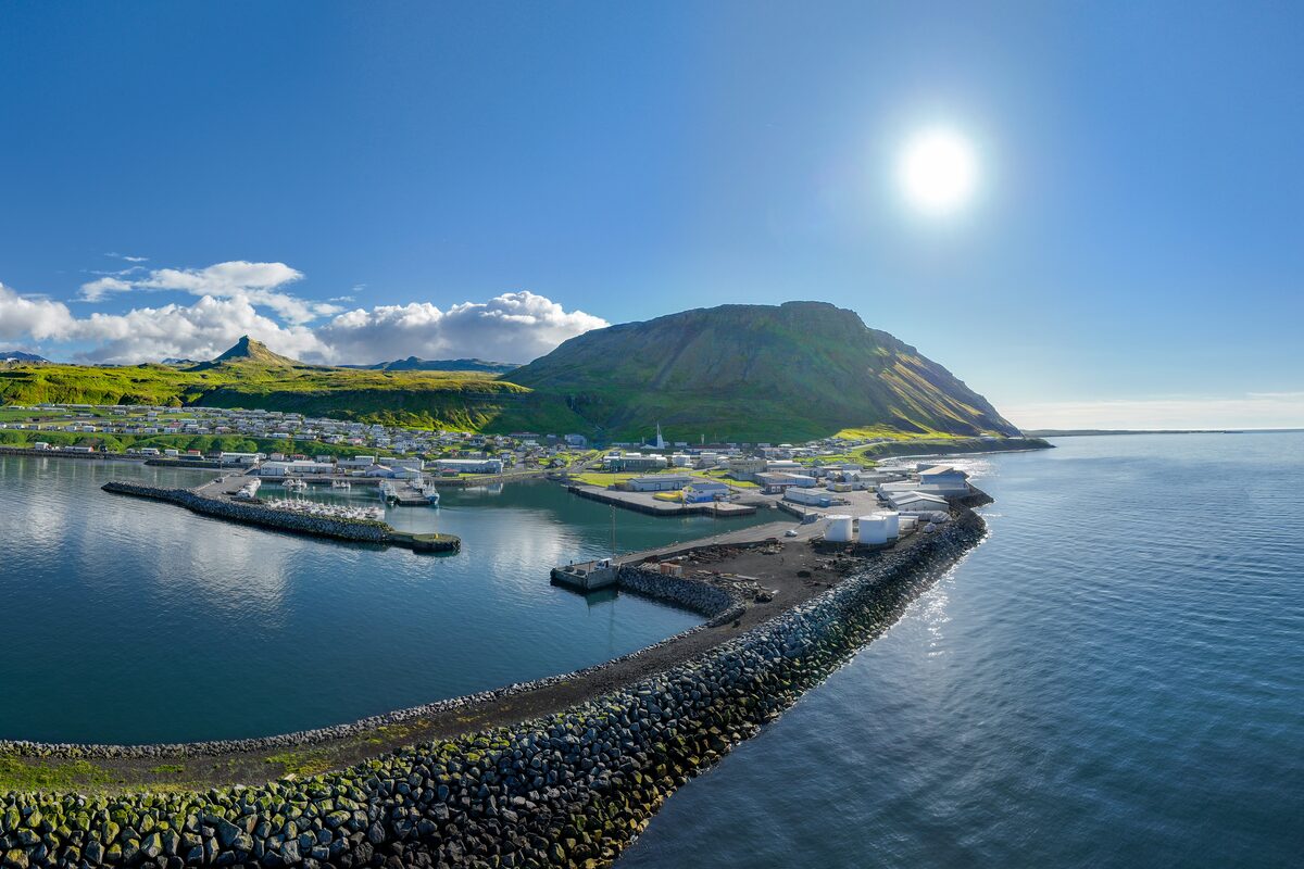 Ólafsvík harbor and town below a green mountain, with a rock breakwater curving into the bay.