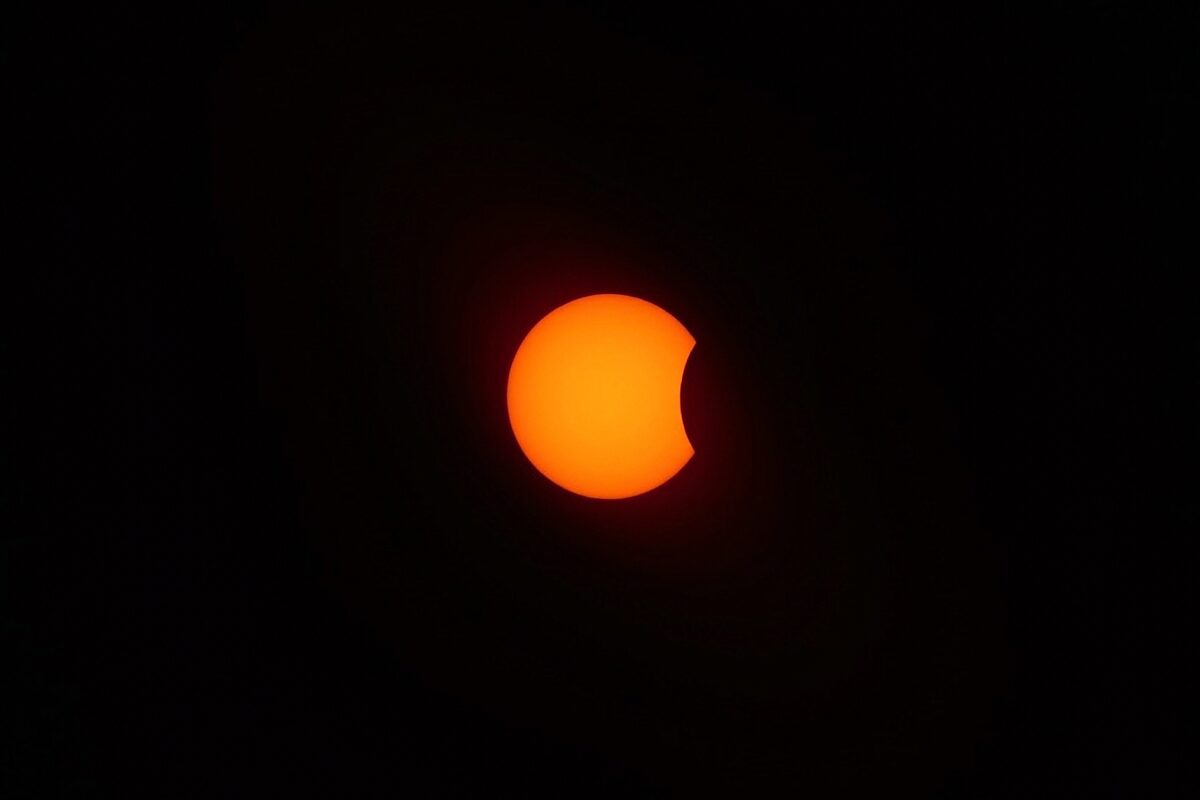 Orange sun with the moon covering its upper edge during the partial eclipse phase.