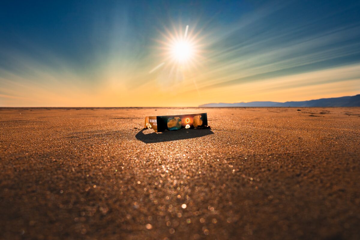 Solar eclipse glasses lying on wet sand with the sun flaring above
