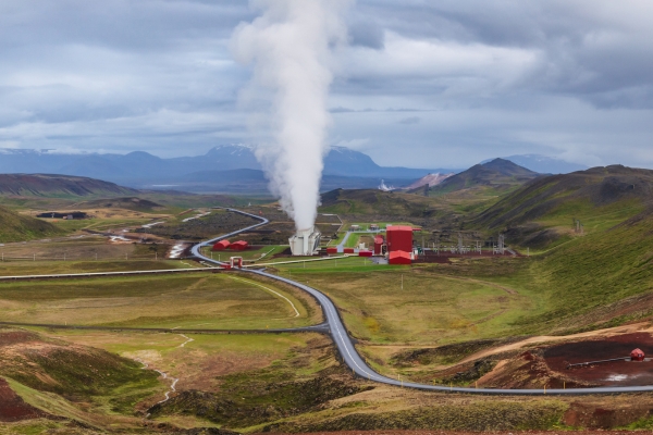 Aerial view of Krafla's power station: red buildings, steam rising, a road winding through hills.