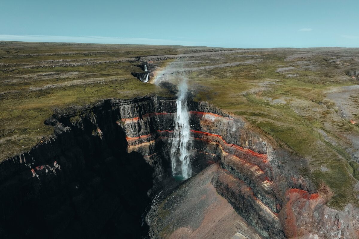 Hengifoss waterfall drops into a layered gorge with red clay bands in East Iceland.