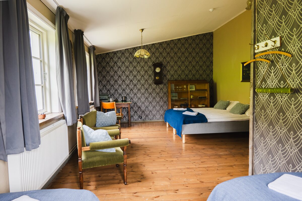 Wilderness Center guest room with beds, green chairs, wooden floors, and patterned wallpaper.