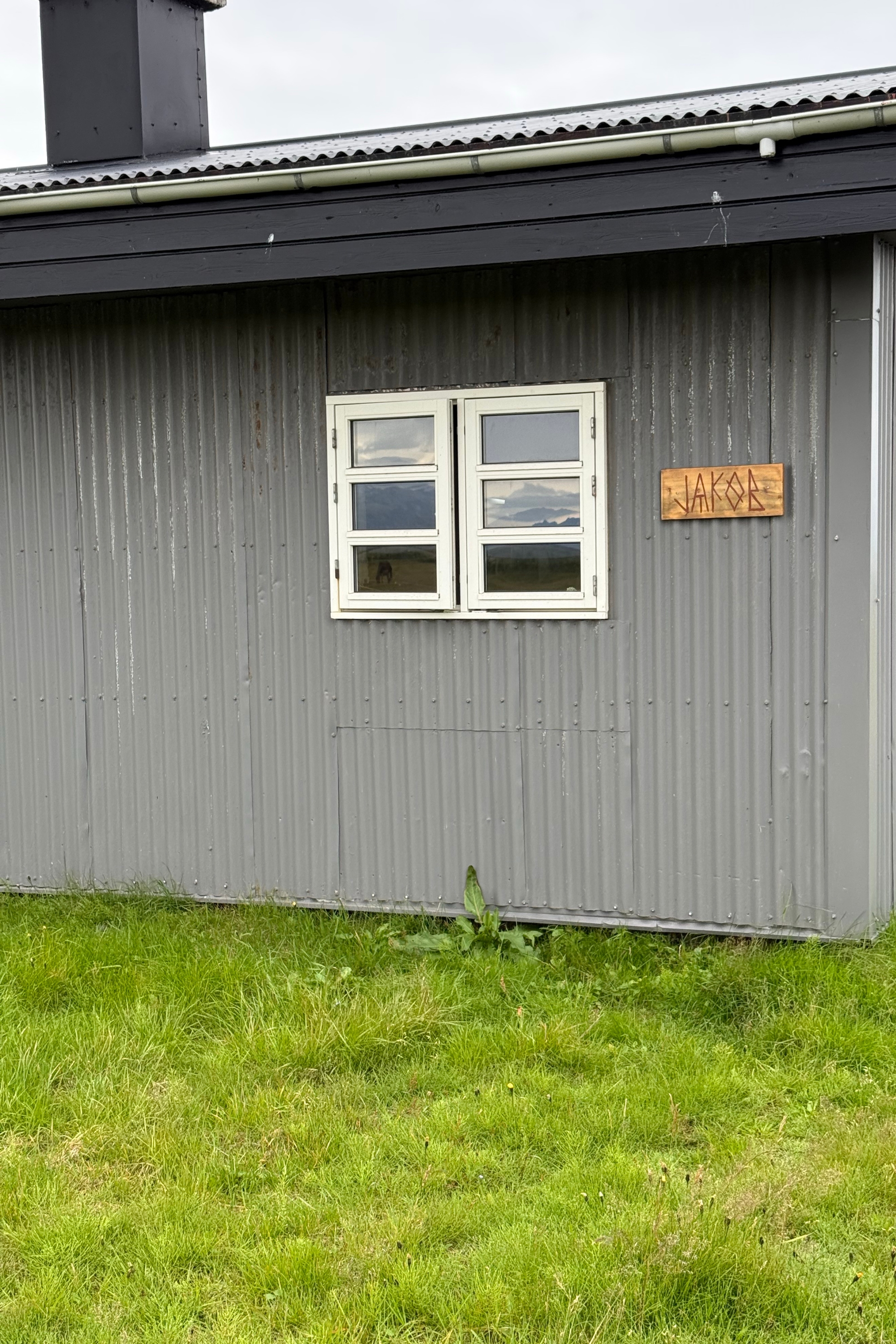 Grey corrugated metal cabin with a white window and a small carved wooden sign.
