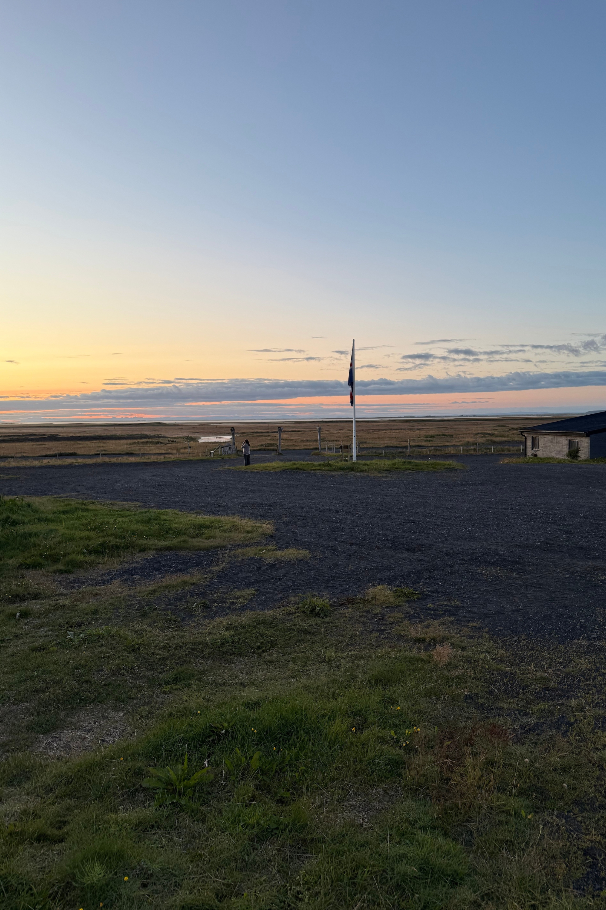 Flagpole on open farmland against an orange and blue sunset sky. 