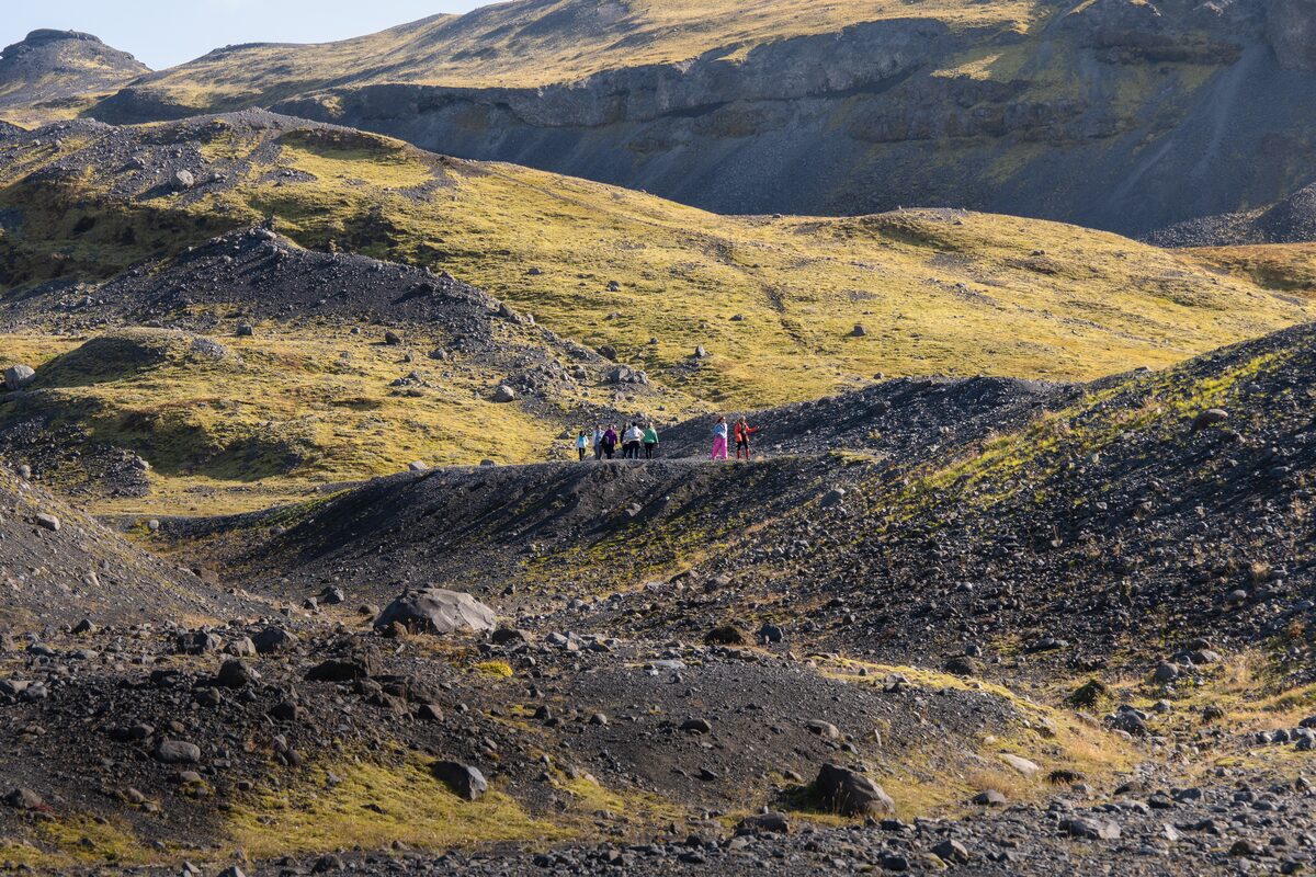 Small group of tourists hiking the moss covered hilly ground surrounding Solheimajokull glacier.