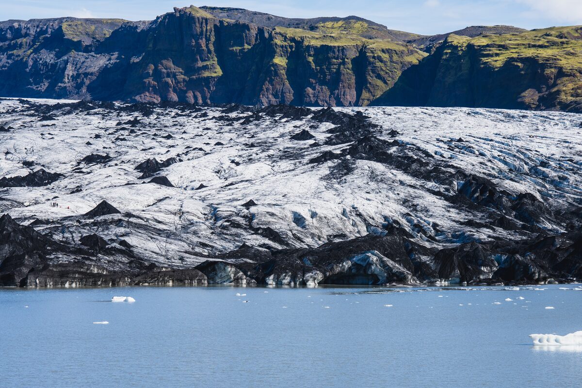 Close up views of Solheimajokull glacial formation with layers of volcanic ash and river in foreground.
