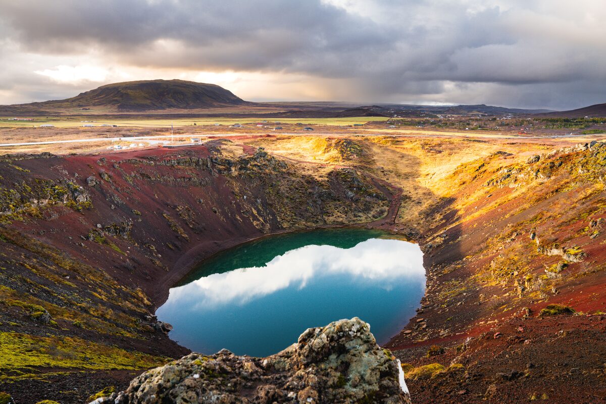 Blue-green lake inside the red volcanic slopes of Kerið crater in South Iceland.