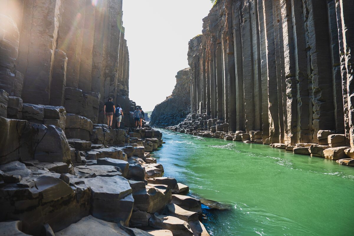 Hikers walking over basalt boulders beside Jökla river in Stuðlagil canyon