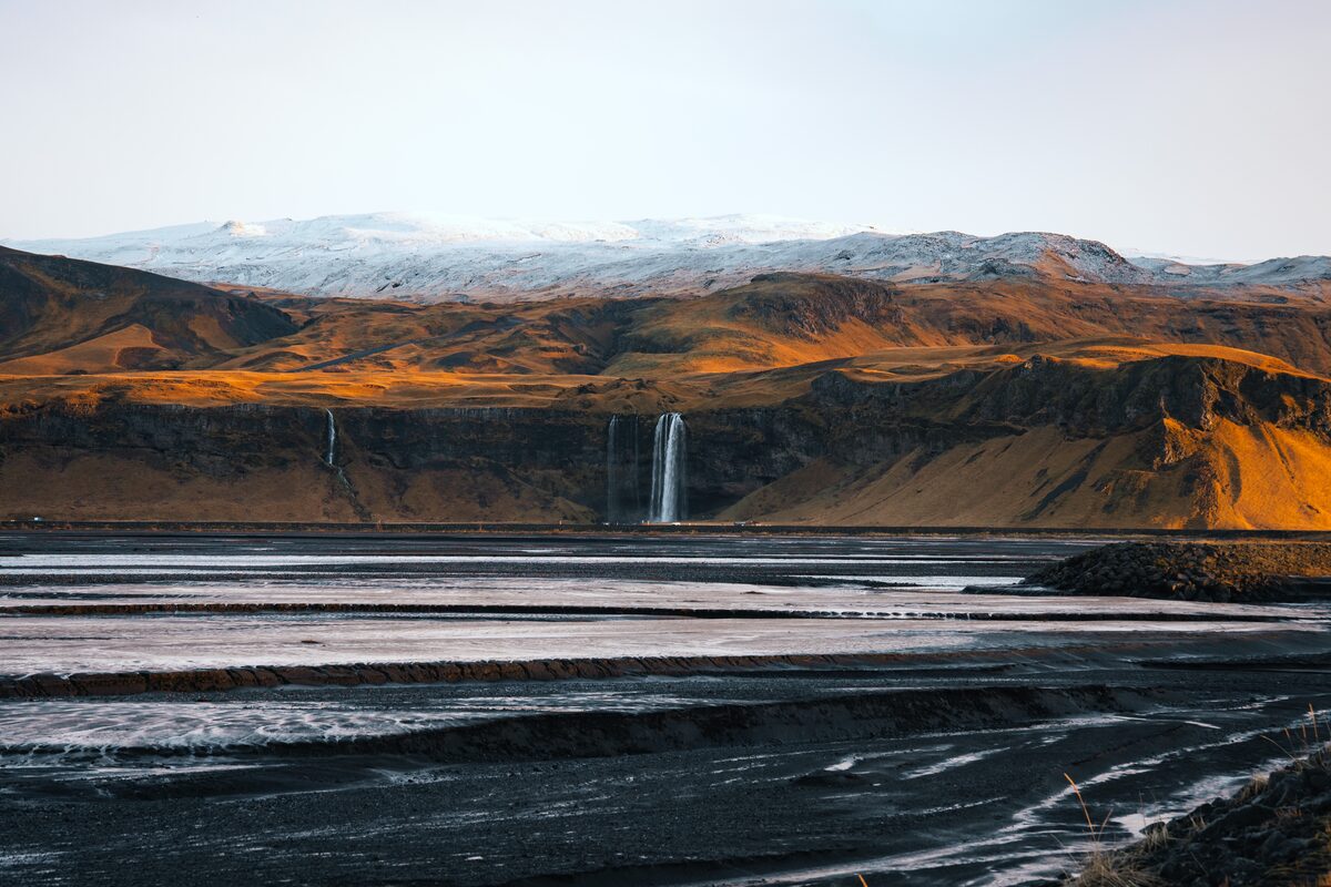 Seljalandfoss waterfall from far away, with views of mountain in winter background.