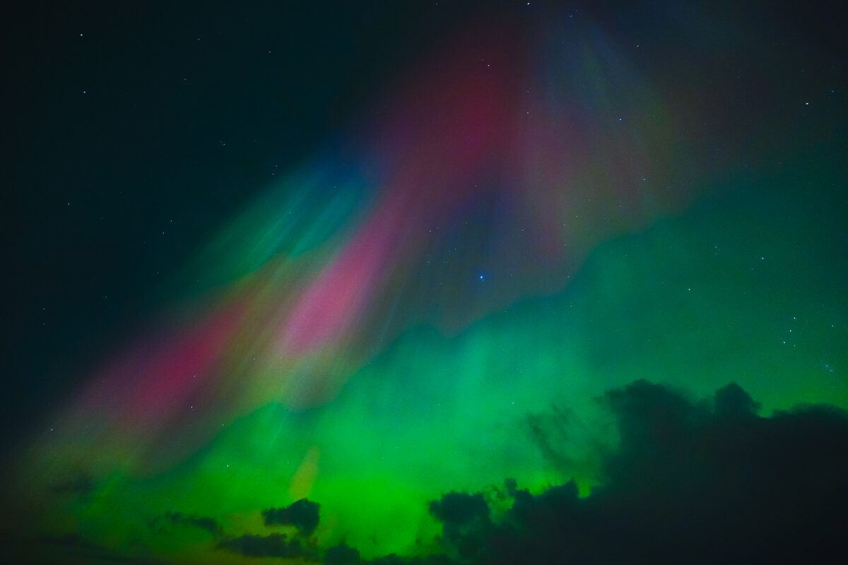 Pink and green aurora bands above dark clouds in the southwest of Iceland.