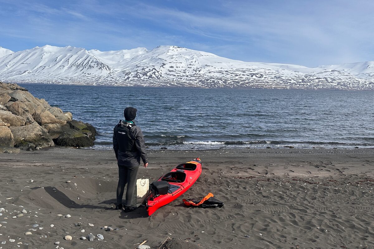 Man Standing Next To A Red Kayak On The Shore in Iceland