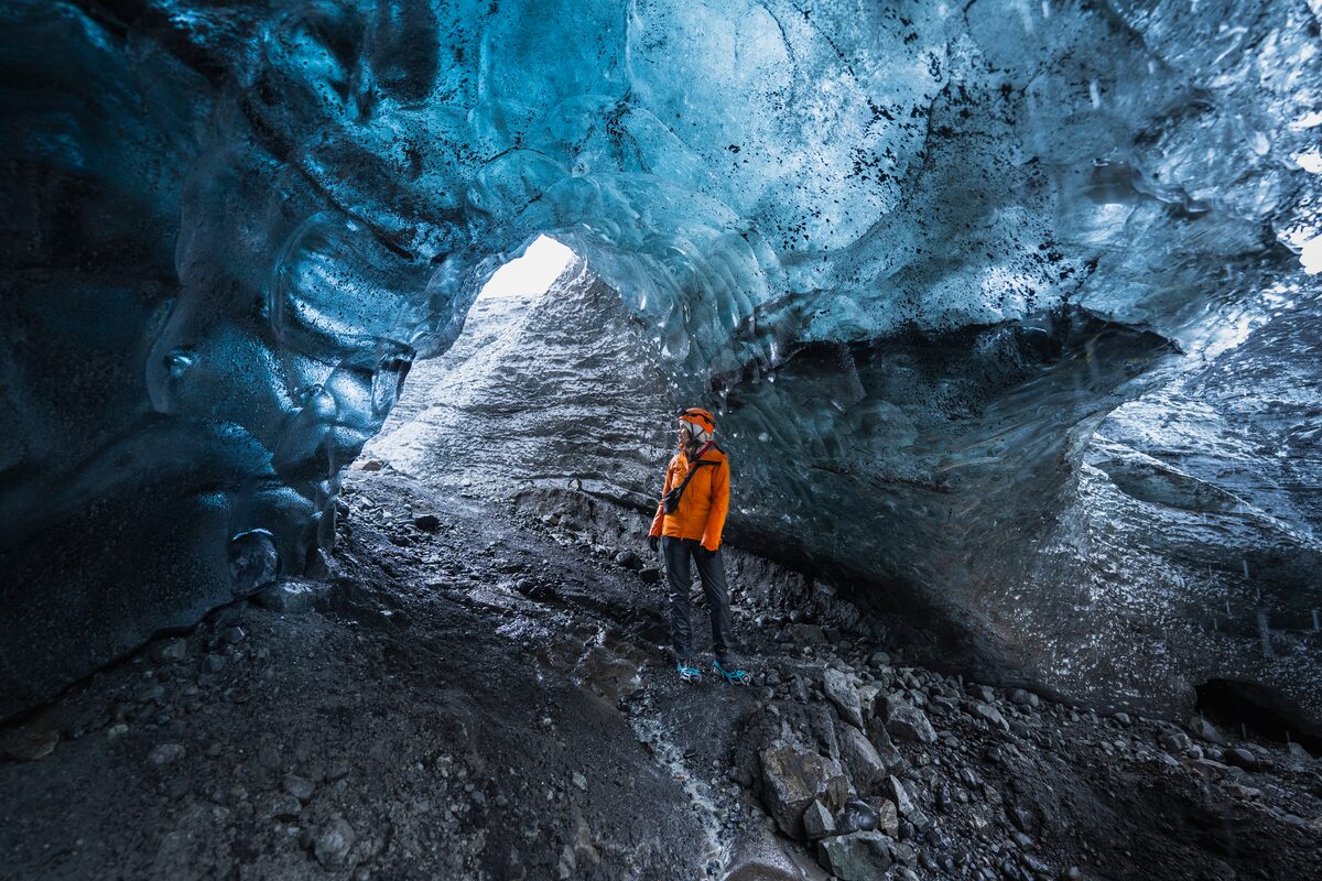 Person standing, posing for photograph inside blue crystal ice cave.