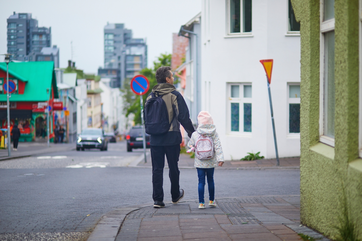 Adult and child walking hand in hand along a residential street in Iceland.