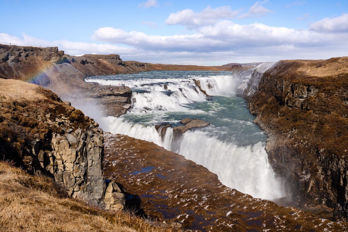 Gullfoss waterfall cascading through a rocky canyon with a rainbow in the spray.