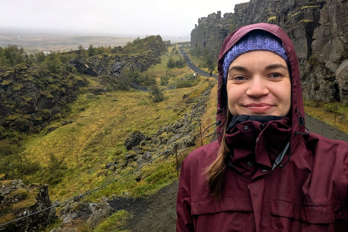Neda Klasinskaitė in a hooded rain jacket at Þingvellir National Park, the rift wall behind her.