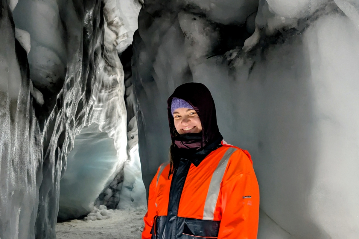 Neda smiling in orange overalls inside an ice tunnel in Langjökull glacier, ice walls around her.