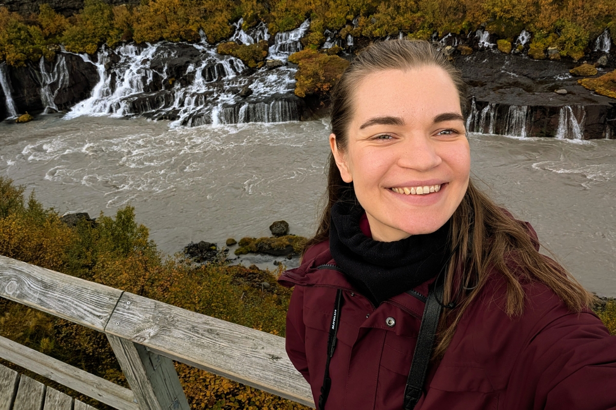 Neda Klasinskaitė taking a selfie above Hraunfossar, with water streaming out of the lava.
