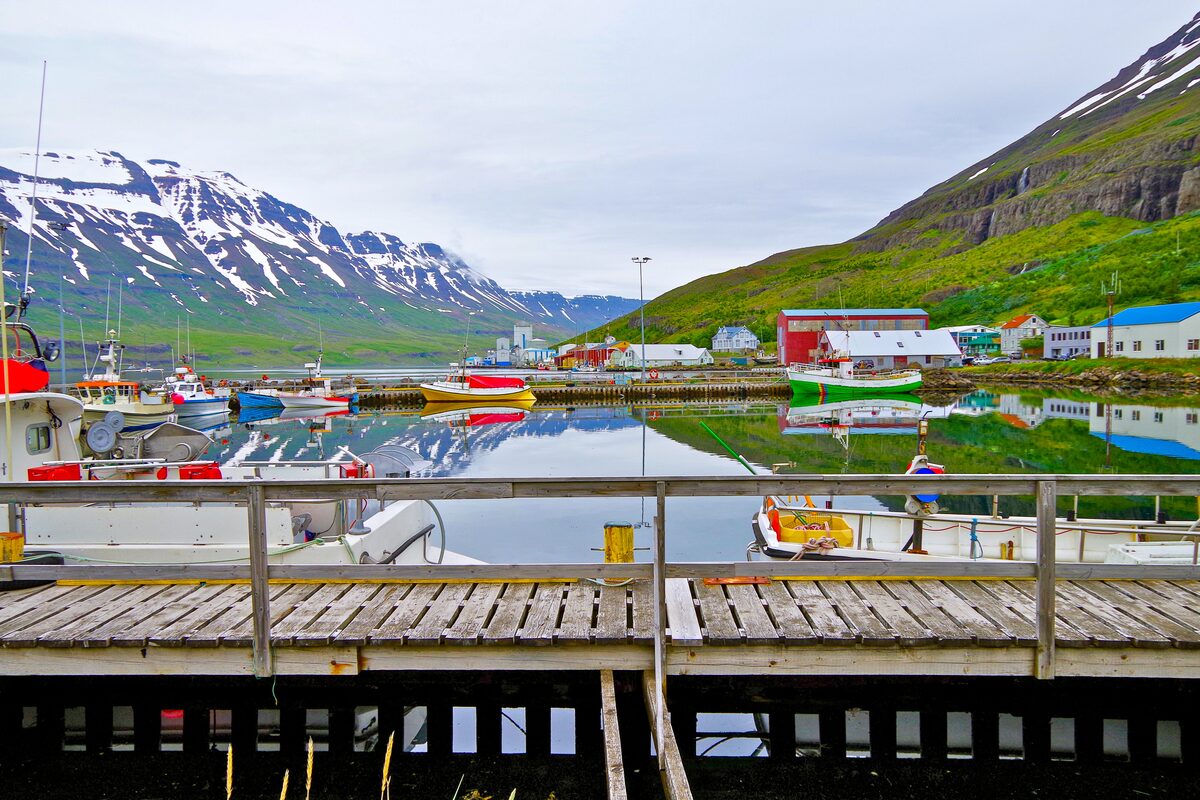 Boats in Seyðisfjörður harbor with snow-streaked mountains reflected in the water.