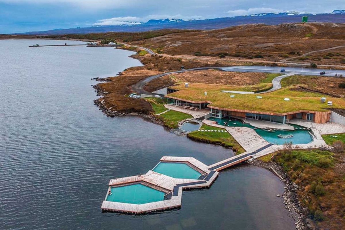 Aerial view of Vök Baths floating pools on Lake Urriðavatn beside a grass-roofed building.