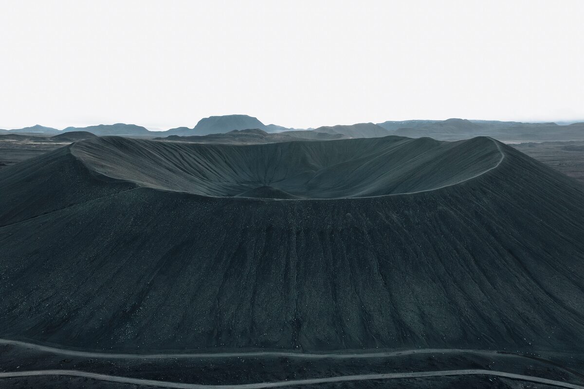 Hverfjall’s dark, near-circular crater seen from outside, with hills beyond.
