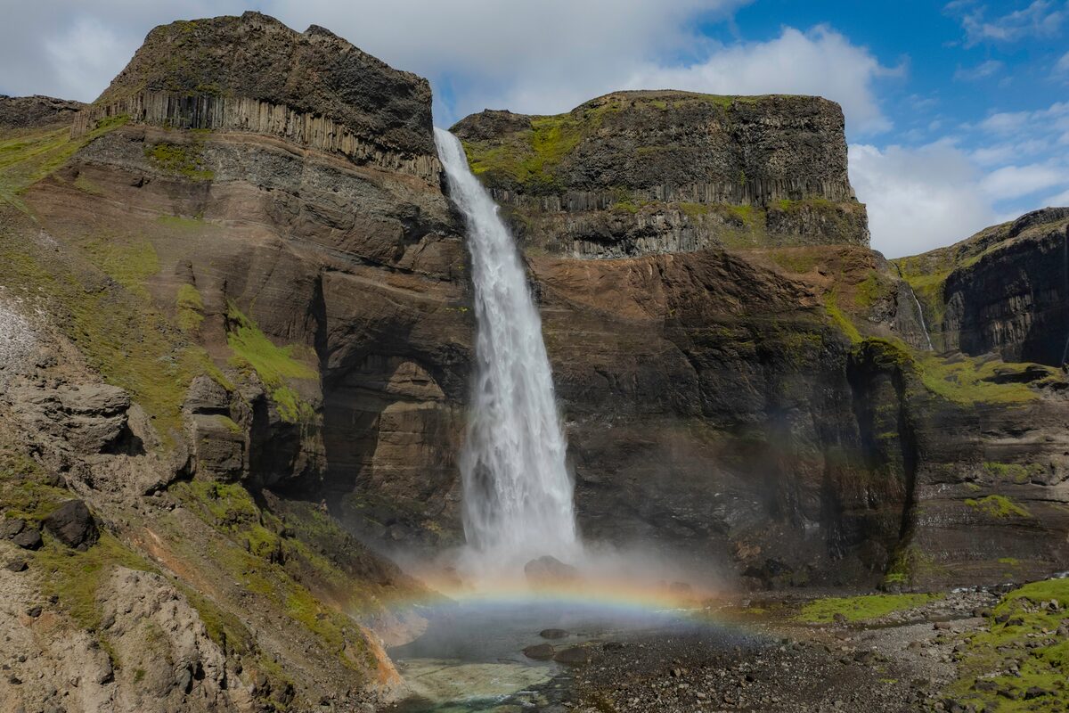 Háifoss waterfall plunging into a pool with a rainbow below layered canyon cliffs.