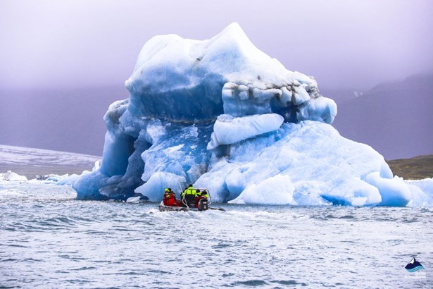 zodiac boat floating near huge iceberg