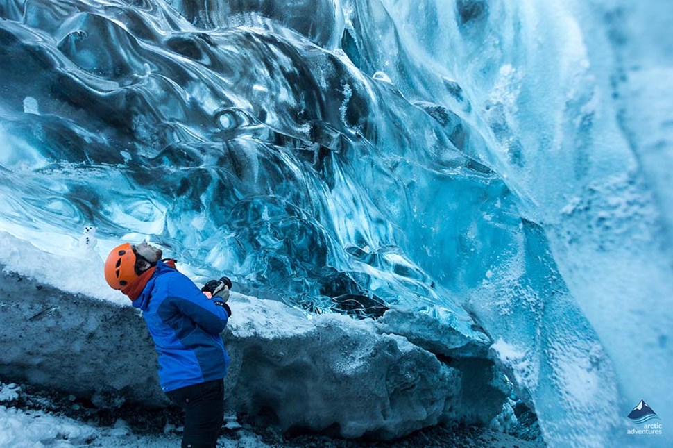 Man in an orange helmet getting an up-close look at the ice formations in an ice cave
